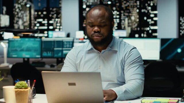 African american analyst pondering about possible outcomes for a problem at workstation after hours, intense concentration to evaluate projections with logical deduction and observation. Camera B.