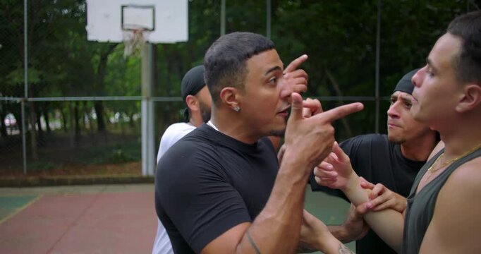 Hispanic men arguing during street basketball game as African descent player steps in to de-escalate conflict, intense emotions and confrontation on court