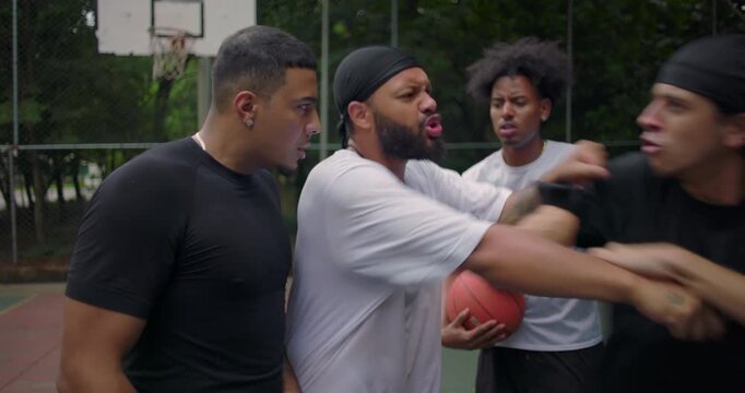 Intense conflict erupts between players during heated street basketball game on outdoor court, as Hispanic man steps in trying to calm situation and stop the fight