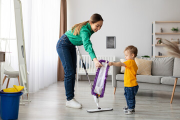 A mother and her young son are engaged in cleaning the floor together. The mother demonstrates how...
