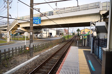 住宅地の踏切の脇にあるローカル線の線路とホームの風景です。頭上には歩道橋や架線があり日本の都市近郊の日常の交通インフラが感じられる情景です。