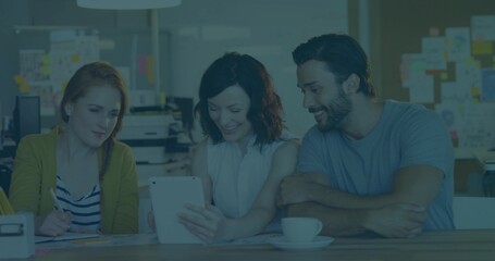 Collaborating trio examining tablet screen at modern office table, with loose papers and coffee