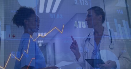 Nurse in scrubs and lab-coated doctor examining chart and tablet in corridor, with floating data