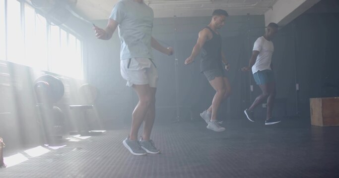 Jumping trio swinging jump ropes in gym in sportswear, weight rack and free weights, plyometric box - Powered by Adobe