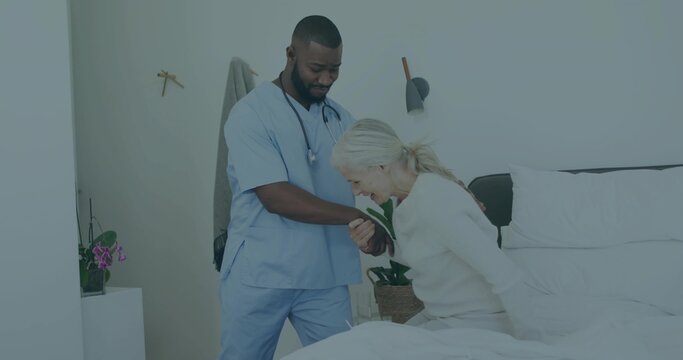 Nurse assisting Senior patient bending forward beside table in bedroom, with scrubs and stethoscope
