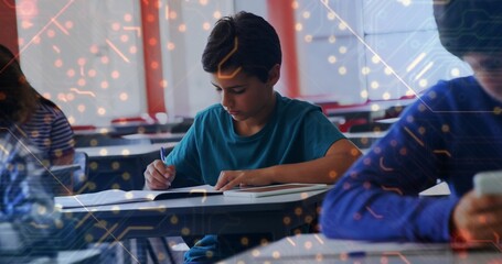 Writing Middle Eastern boy focusing on penning notes at individual school desk, with notebook, pen