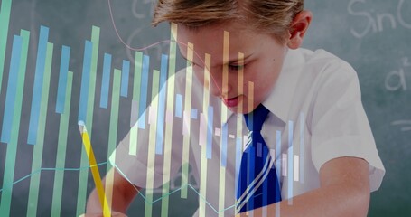 Writing schoolboy using yellow pencil at classroom desk with chalkboard and digital chart overlays