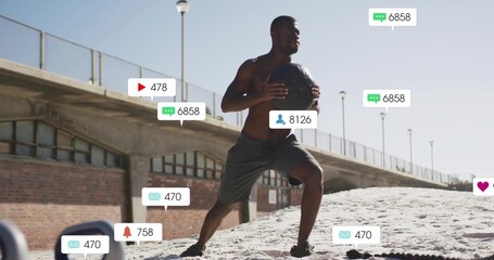 Lunging athlete wearing shorts twisting holding medicine ball on sandy beach, with floating icons