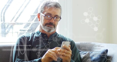 Senior man with green shirt, glasses, tapping smartphone on gray sofa at home, with data overlays