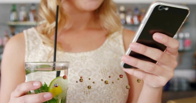 Sipping cocktail with straw and holding smartphone, blonde woman in lace top at bar counter