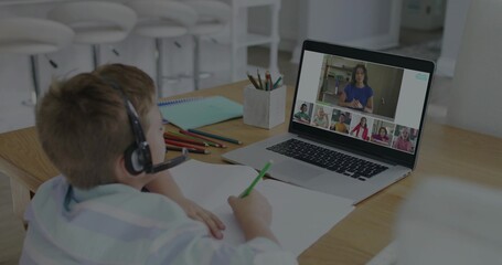 Studying boy wearing striped shirt and headset at kitchen table with laptop, pencils, copy space