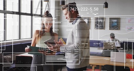 Office colleagues discussing data overlays by floor-to-ceiling windows, with clipboard and tablet