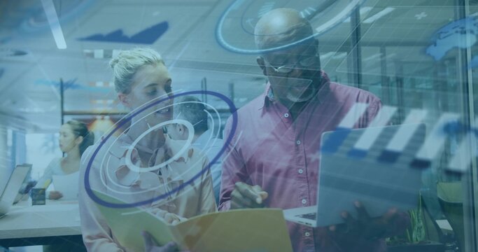 Analyst and consultant in office attire reviewing display at desk, with yellow folder and laptop