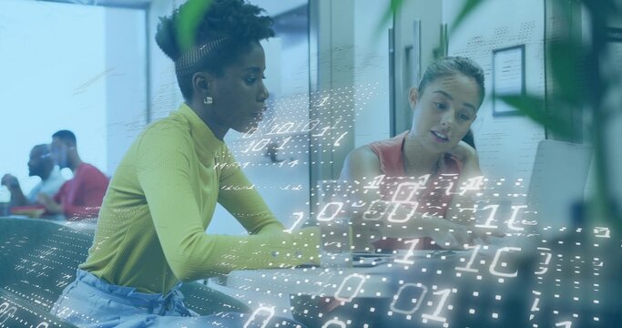 Collaborating two office workers reviewing laptop screen at office desk, with binary code overlay