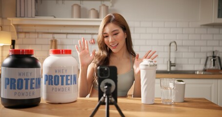 Young Asian female health influencer live streaming on social media sharing nutrition tips with whey protein powder by smartphone. Healthy lifestyle, fitness coaching, clean eating. online marketing.