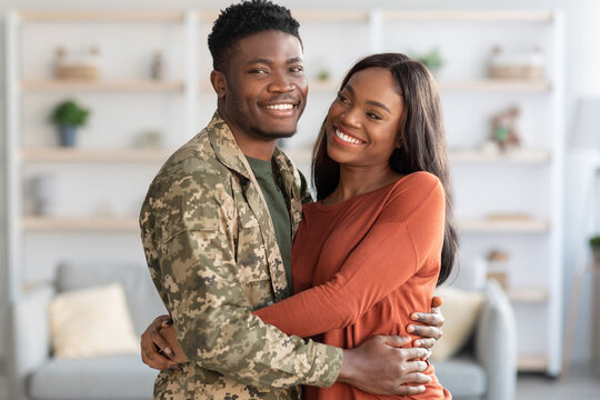 A man in military uniform and a woman in a casual outfit share a joyful moment together at home. They are smiling and hugging, celebrating their time together after deployment.