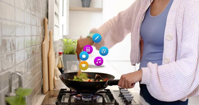 Mid adult woman stirring noodle stir-fry in kitchen, generating category icons orbiting wok fading