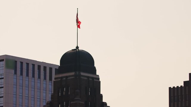 Red And White Canadian Flag Flutters In The Wind Against The Sunset Sky In Halifax Nova Scotia, Canada, With The Smaller Flag On A Skyscraper Tower In The Background.