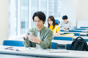 教室でスマホを見る大学生
