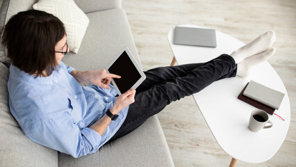 A person sits comfortably on a gray couch, engaged with a tablet. Nearby, a coffee cup, notebook,...
