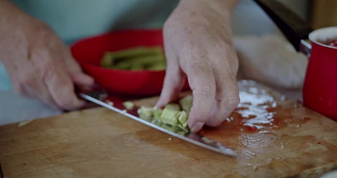 A close-up view of hands skillfully chopping fresh green okra on a rustic wooden cutting board. This highlights the careful preparation of healthy, homemade vegetables for a nutritious meal.
