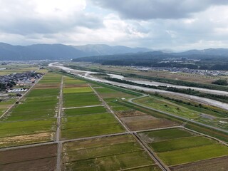 A large field of green grass with a river running through it. The sky is cloudy and the landscape is peaceful