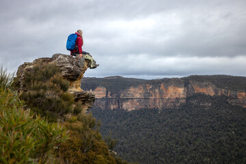 Female hiker sits high up on a rock precipice overlooking mountains