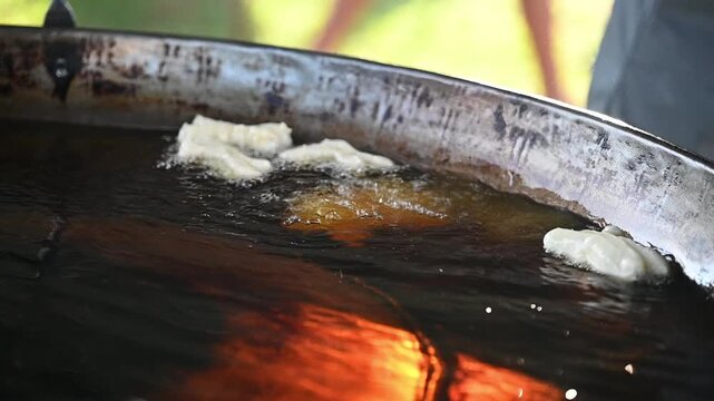 street food deep fried dough vendor hot oil outdoor market ladle golden crispy snack breakfast slow motion video capture shows fresh dough lifted from bubbling oil with steam and slight drizzle evokin