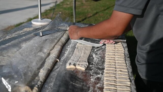 Handmade dumpling dough street food outdoor market artisan cooking flour dust rustic table natural light closeup texture slow motion video culinary craft fill frame with calm focus hand dough cutter