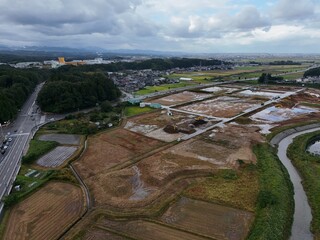 A view of a rural area with a river running through it. The land is mostly dry, but there are some areas that are flooded. The sky is cloudy, and there are some trees in the background
