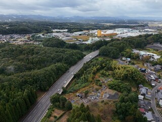 A view of a city with a highway and a bridge in the middle. The highway is busy with cars and trucks. The bridge is tall and has a yellow color. The city has a lot of buildings and houses