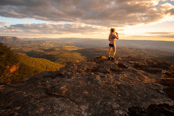 Woman on rock with drink looking at mountain valley views
