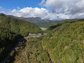 A mountain range with a forest in the background. The sky is cloudy and the sun is shining