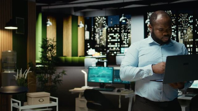 Black guy examining archived documents before transcribing on pc notebook, notetaking and extracting the main points from reports on laptop. Analyst documenting after hours late at night. Camera A.