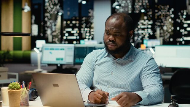 Black office employee ripping a piece of paper after making a mistake, restarting his task in anger and tearing up the page sheet. Discontent guy writes a typo while transcribing. Camera B.