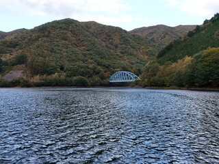 A bridge spans a large body of water, with mountains in the background. The bridge is blue and white, and the water is calm