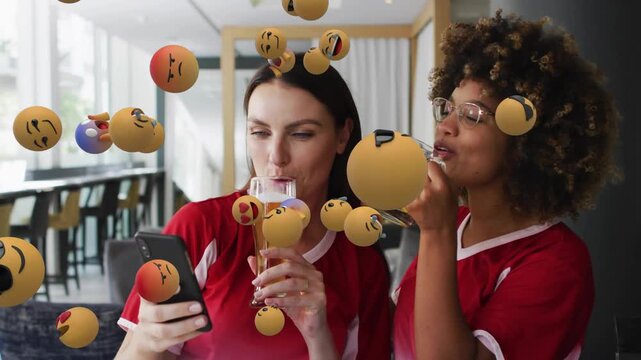 Two friends at bar tapping smartphone reacting and causing emoji spheres swirling around drinks