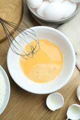 Beaten eggs in bowl and whisk on wooden table, flat lay