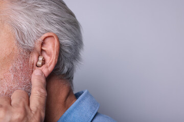 Fototapeta premium Senior man with hearing aid on light grey background, closeup