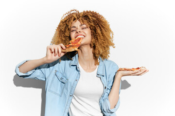 Joyful young woman enjoying pizza against a bright background, wearing a denim jacket, showcasing...