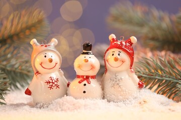 Cute decorative snowmen and fir tree branches on artificial snow against blurred background, closeup