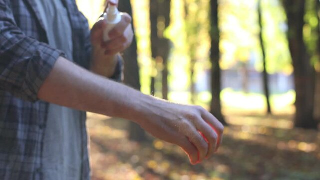Man spraying tick repellent onto arm in park, closeup