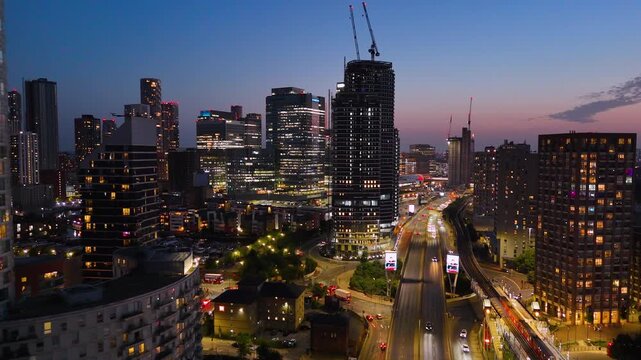 Night aerial views of London&rsquo;s skyline, showcasing illuminated towers, highways, trains, and vibrant urban lights during twilight. Cinematic city atmosphere.