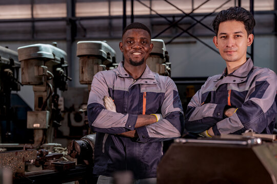 Two confident industrial technicians standing in a machine workshop with arms crossed. Teamwork, skilled labor, engineering, manufacturing, and industrial pride.