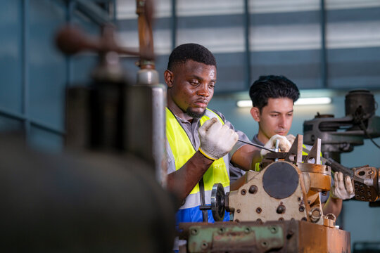 Two engineers focus on adjusting industrial machinery with precision. Teamwork, mechanical engineering, machine maintenance, technical collaboration, and industrial training. - Powered by Adobe
