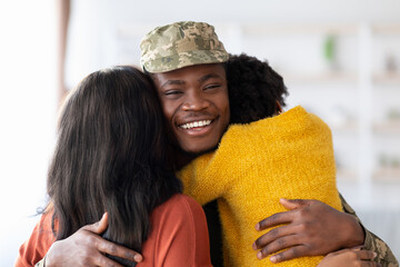 A soldier in military uniform is warmly embraced by two family members. The joyful atmosphere...