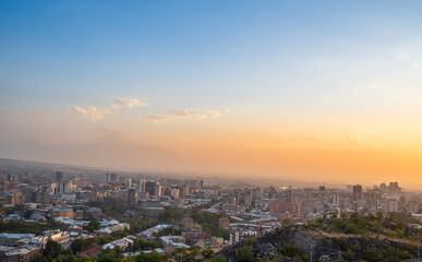 Aerial view of Yerevan, Armenia at sunset with Mount Ararat visible in the distance. The sky shows a beautiful gradient from blue to orange, highlighting the city’s skyline