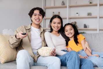 Obraz premium Three family members enjoy a cozy movie night at home, sharing popcorn and smiles while watching their favorite film together in a comfortable living room.