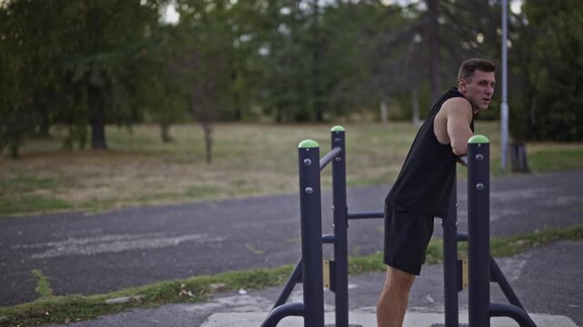 An athletic man performs an intense core workout on parallel bars in an outdoor park gym. This dynamic exercise showcases dedication to fitness and a healthy, active lifestyle.
