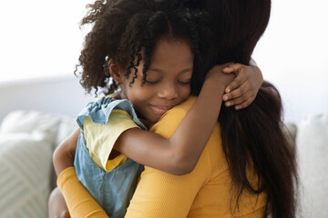 A young girl embraces her mother with joy, showcasing a strong bond between them. The cozy indoor setting enhances the warmth of their loving interaction.